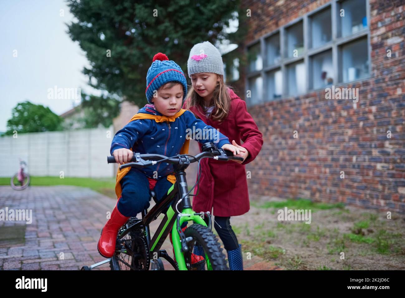 Non ti lascerò cadere. Scatto corto di una bambina che insegna a suo fratello come andare in bicicletta fuori. Foto Stock