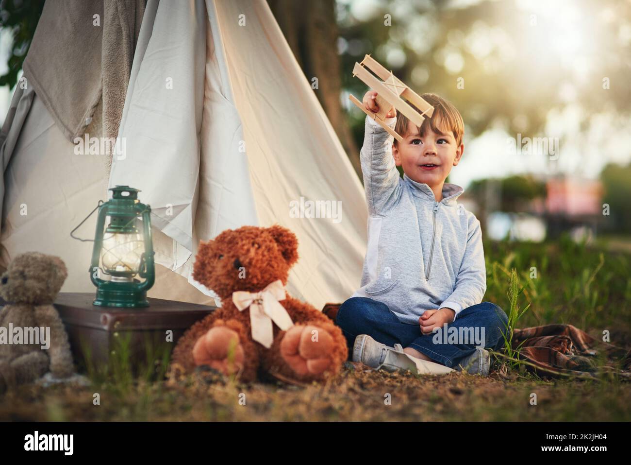 Si alza sopra le nuvole. Scatto di un ragazzino carino che gioca con un aeroplano giocattolo mentre si siede al di fuori della sua teepee. Foto Stock