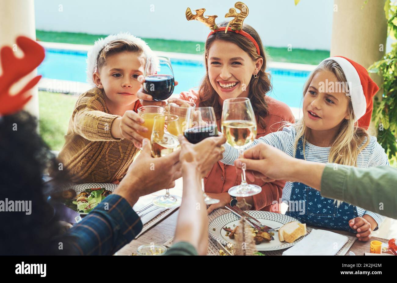 Buon Natale a tutti. Scatto di una bella giovane famiglia che unisce i loro bicchieri per un brindisi a un pranzo di Natale festa. Foto Stock