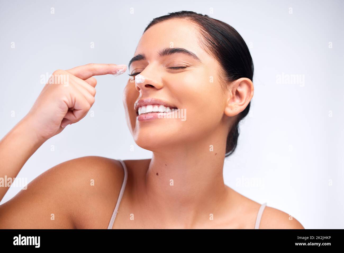 Non lasci la vostra pelle alta e asciutta. Scatto di una bella giovane donna che applica moisturizer al suo viso. Foto Stock