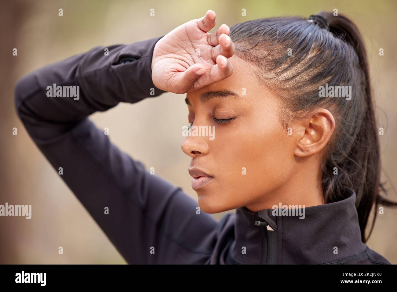 Le emicranie possono rovinare tutti i programmi. Shot di una giovane donna che sperimenta un mal di testa mentre fuori jogging nella foresta. Foto Stock