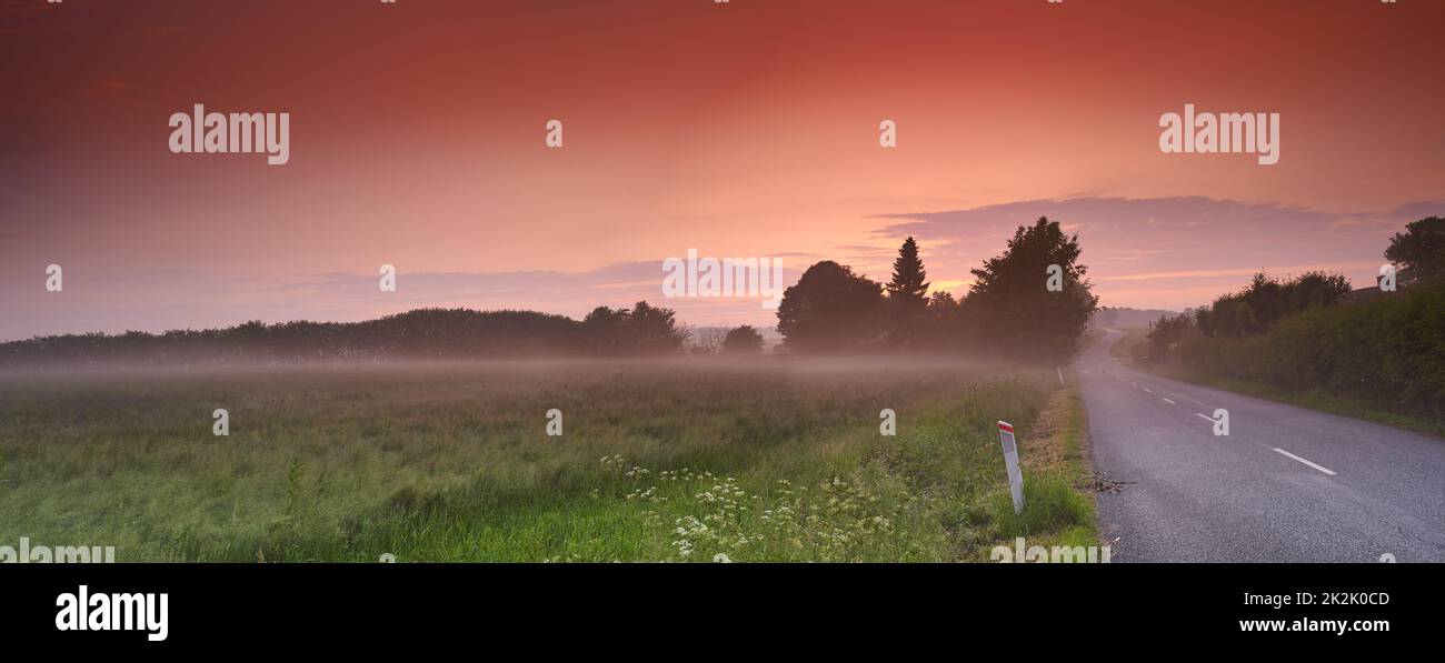 Viaggio panoramico al tramonto. Una strada attraverso un paesaggio idilliaco con il sole che tramonta all'orizzonte. Foto Stock