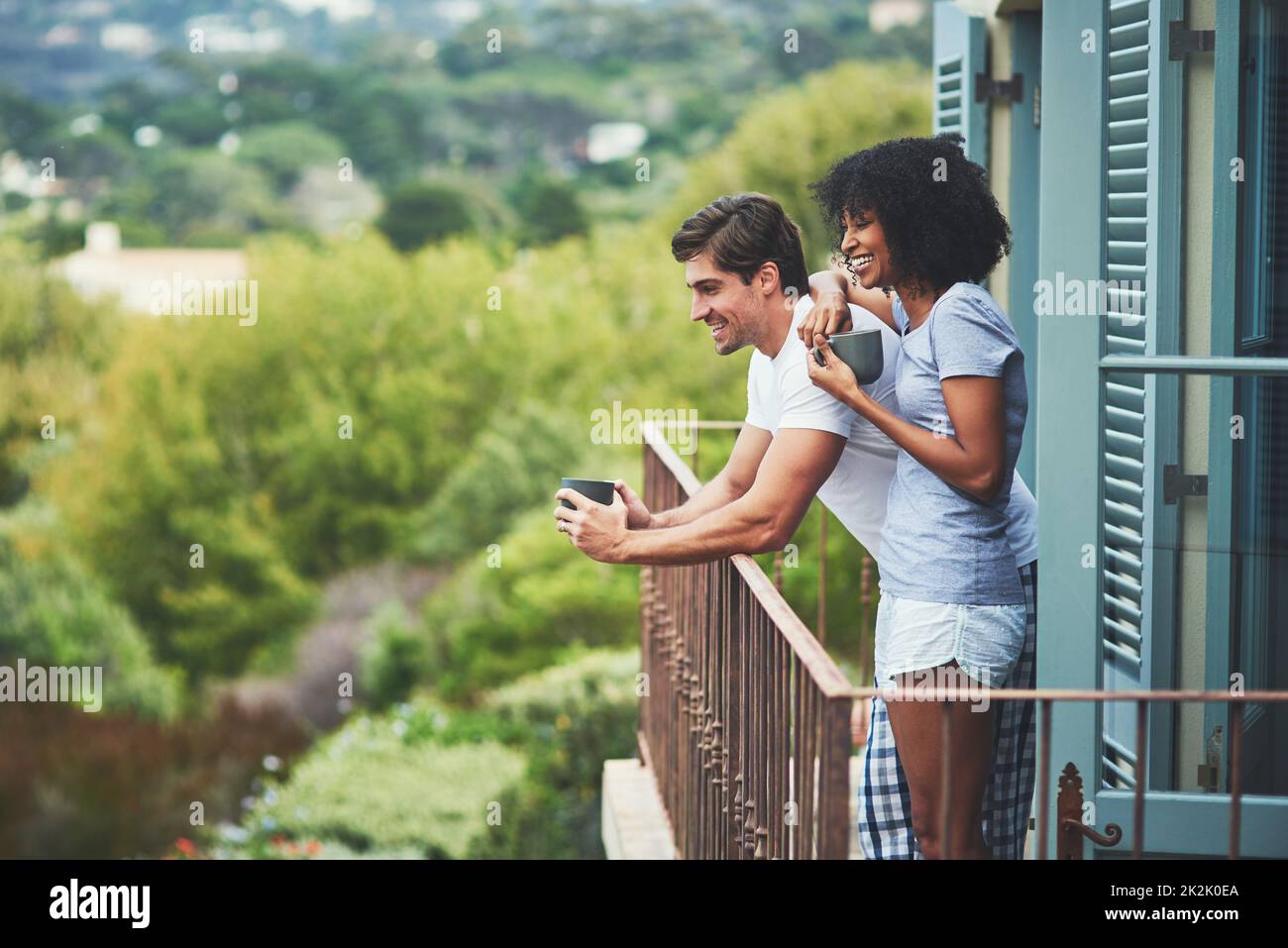 Questo posto è semplicemente incredibile. Shot di una giovane coppia affettuosa bere caffè e guardare la vista mentre si trova su un balcone a casa. Foto Stock