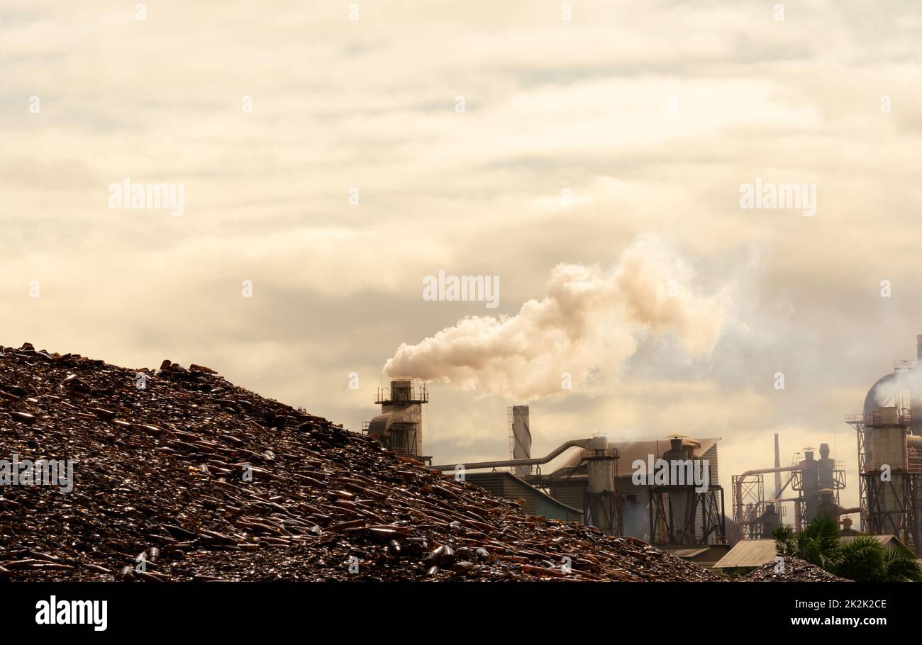 Pila di bottiglie marroni per il riciclo in fabbrica. Rifiuti di vetro per riciclaggio. Emissioni di CO2. Emissioni di anidride carbonica di gas serra dai camini delle fabbriche. Fumo da camini. Concetto di inquinamento atmosferico Foto Stock