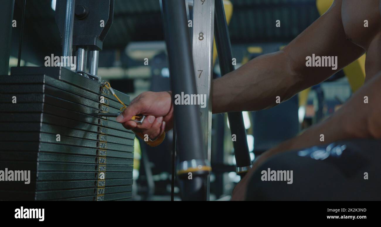 Mani di primo piano di atleta uomo sceglie il peso nelle attrezzature sportive in macchina ginnica Foto Stock