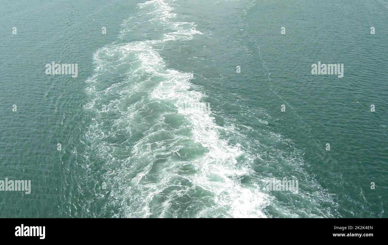 Un sentiero spumeggiante e gorgogliante sulla superficie azzurra dell'acqua dal movimento di una grande nave in mare Foto Stock