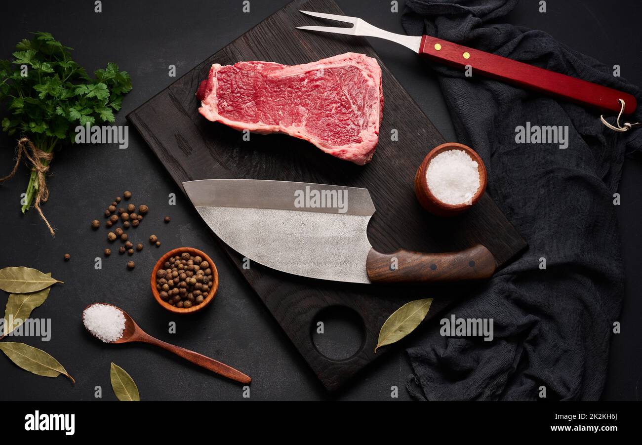 Pezzo fresco di carne di manzo cruda, bistecca di striploin su sfondo nero, vista dall'alto Foto Stock