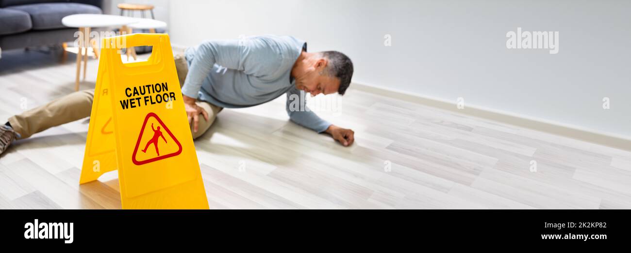 Uomo che cade sul pavimento bagnato di fronte al cartello di attenzione Foto Stock