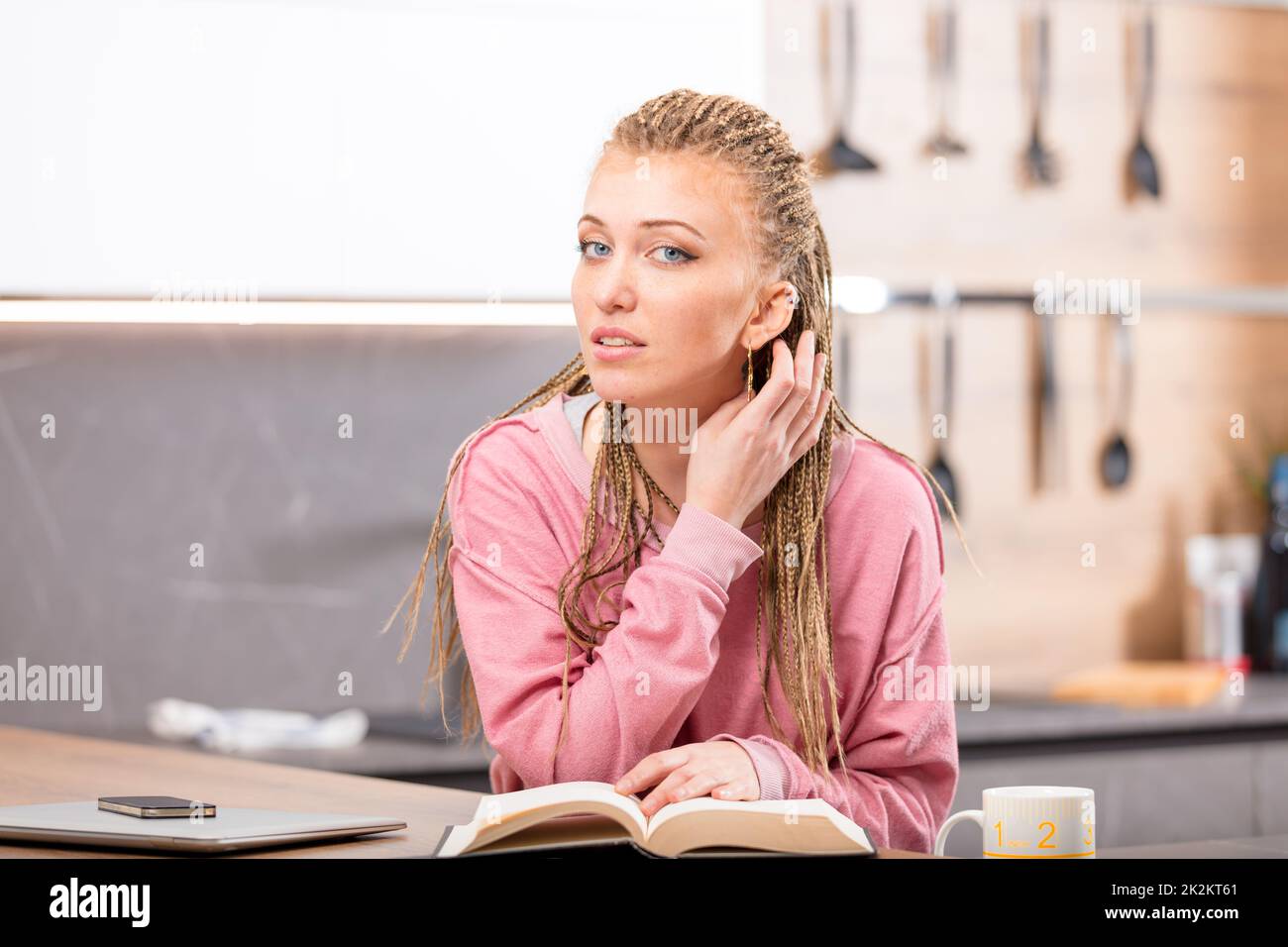 Giovane donna dai capelli lunghi seduta con libro a tavola Foto Stock