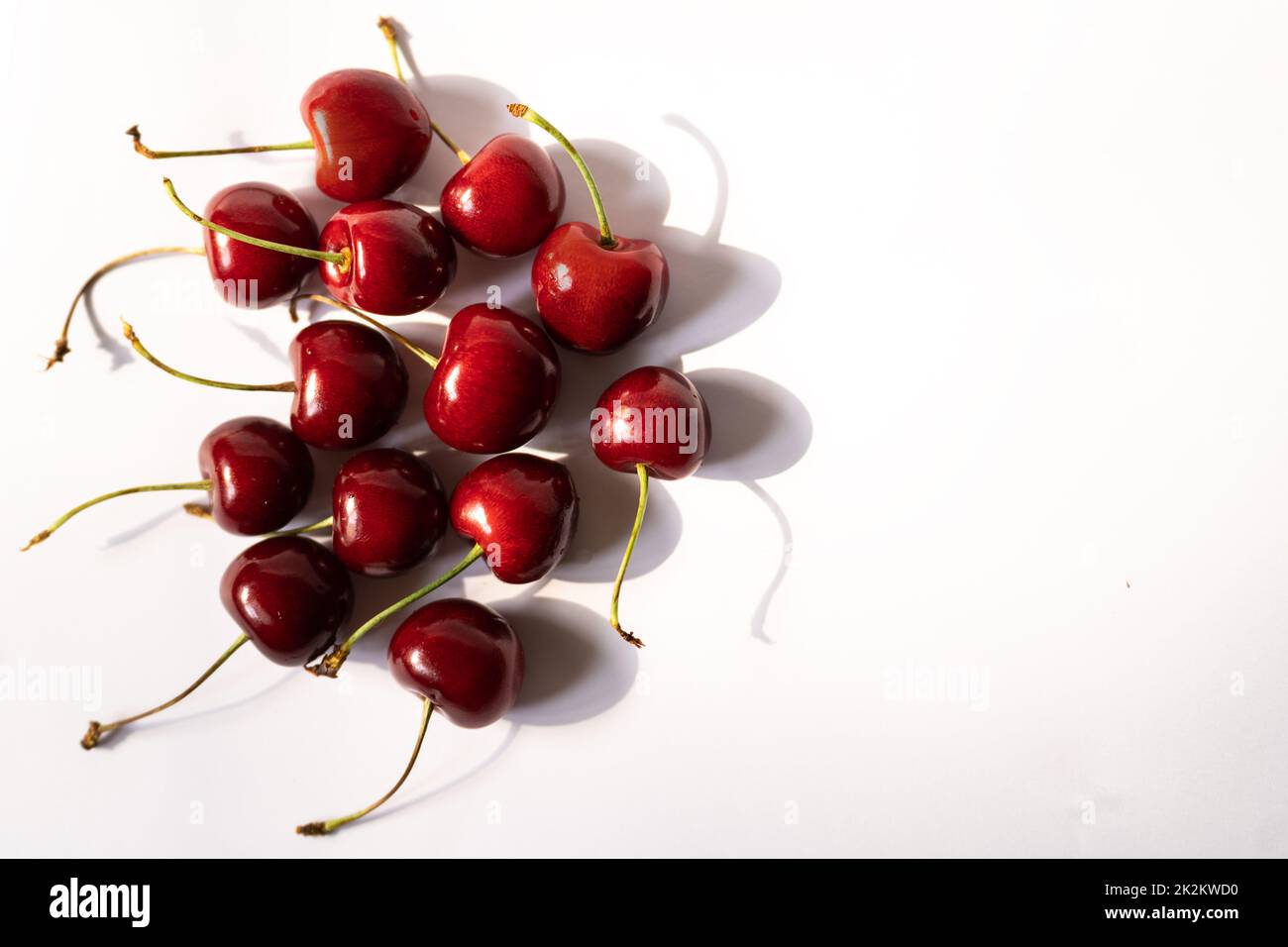 Le ciliegie con germogli hanno ombre dure, poste in un mazzo su uno sfondo chiaro Foto Stock