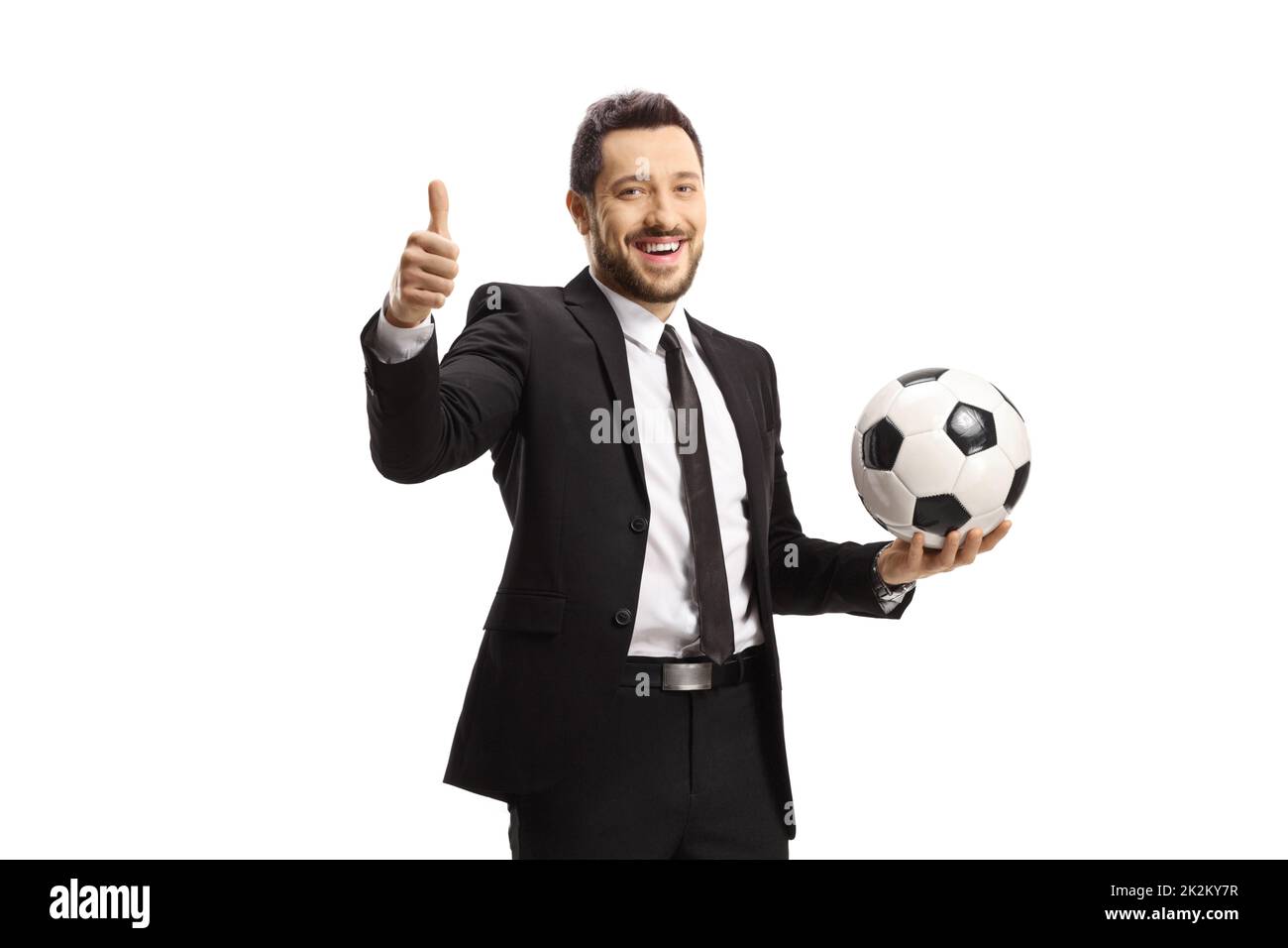 Uomo allegro in una tuta nera che tiene un calcio e mostra i pollici isolato su sfondo bianco Foto Stock
