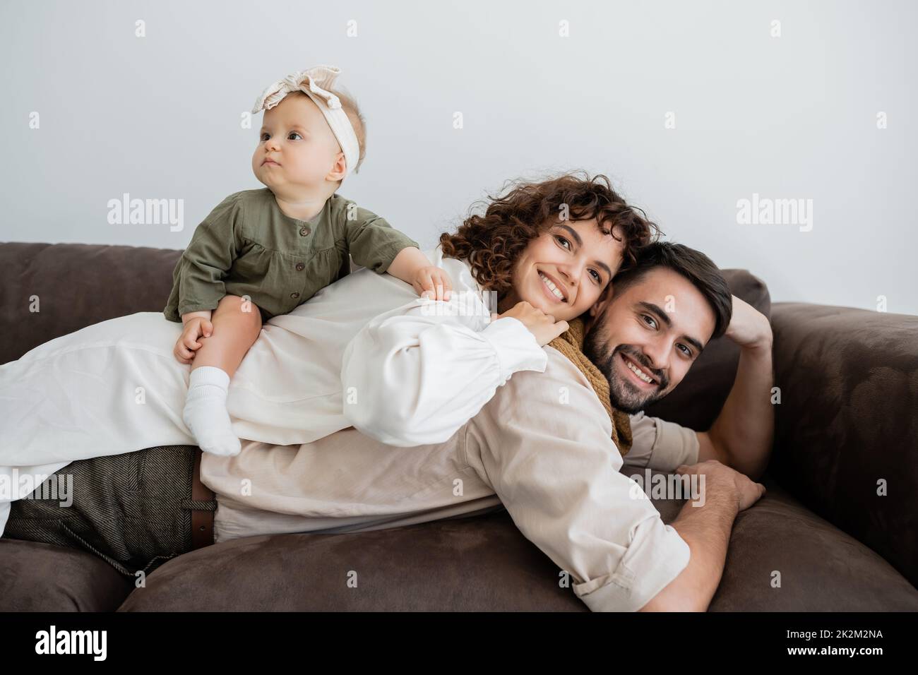 donna allegra e riccia e ragazza bambino sdraiata sulla schiena del marito bearded in soggiorno, immagine stock Foto Stock