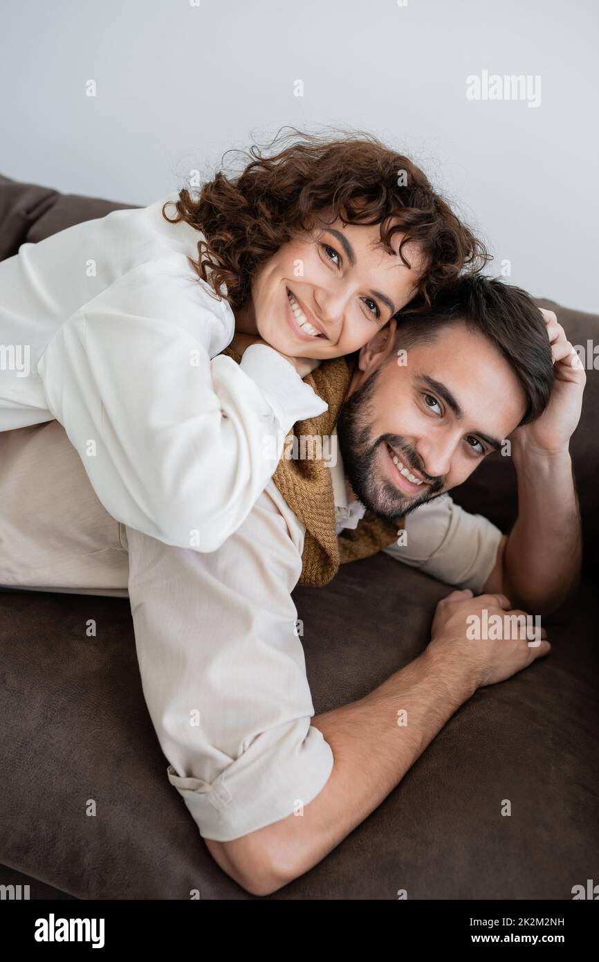 donna felice e riccia sdraiata sulla schiena di marito bearded sul divano, immagine stock Foto Stock