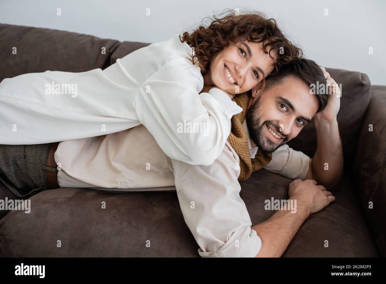 donna allegra e ricciola sdraiata sul dorso di un marito bearded sul divano, immagine di scorta Foto Stock
