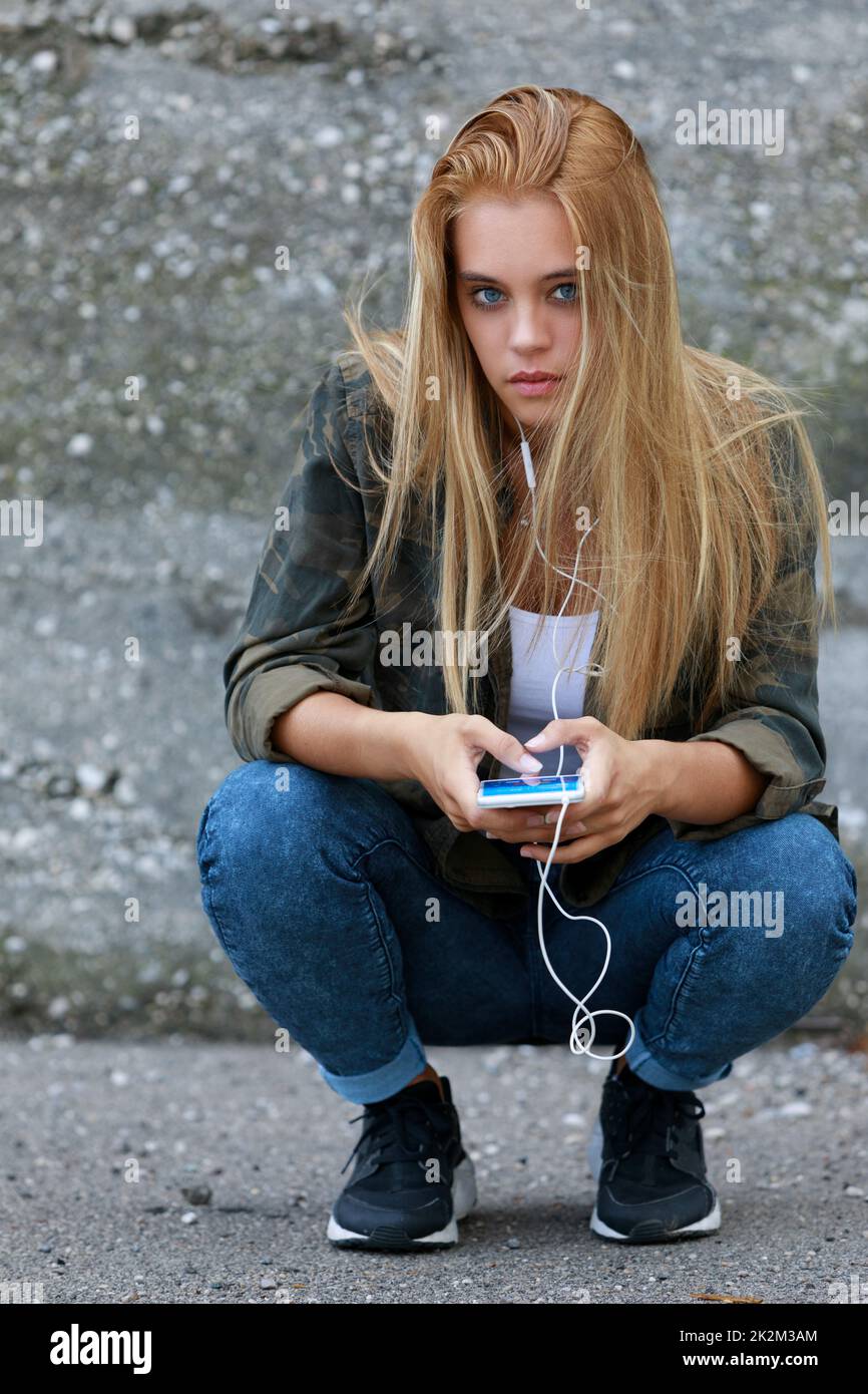 bella ragazza bionda che ascolta musica con il suo smartphone in città, fissandovi Foto Stock
