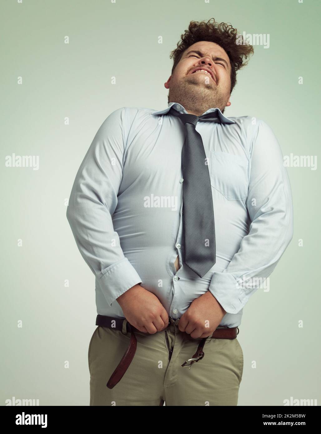 Volendo i suoi pantaloni chiusi. Humorous studio girato di un uomo d'affari overweight che prova a premere i suoi pantaloni. Foto Stock
