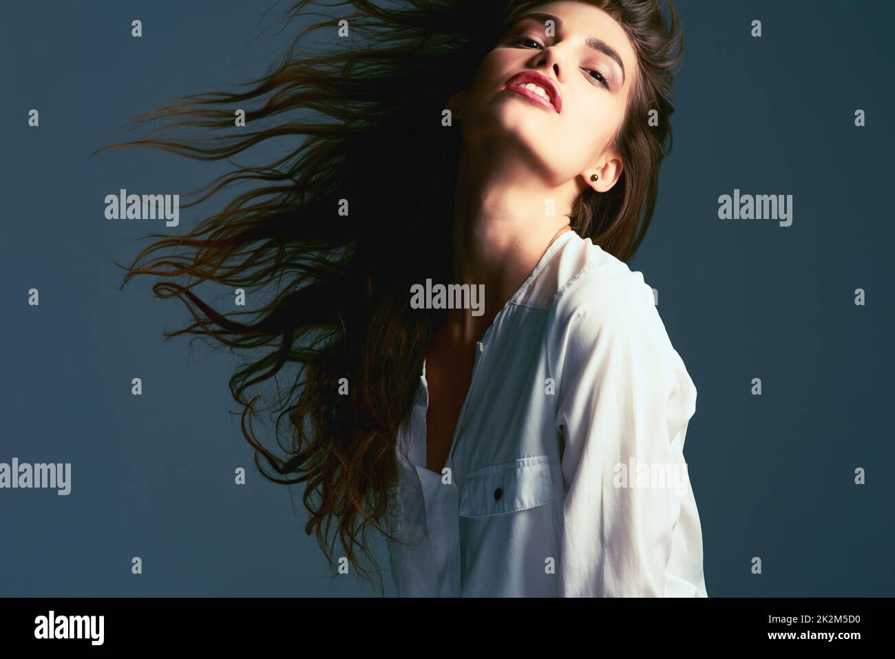 Montare i capelli avanti e indietro. Studio girato di una giovane attraente donna alla moda in posa su uno sfondo blu. Foto Stock