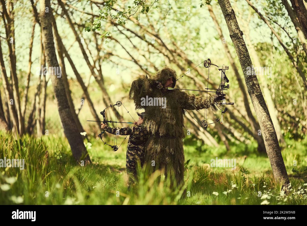 Tutto su AIM. Sparato di padre e figlio in camouflage caccia con archi e frecce nei boschi. Foto Stock