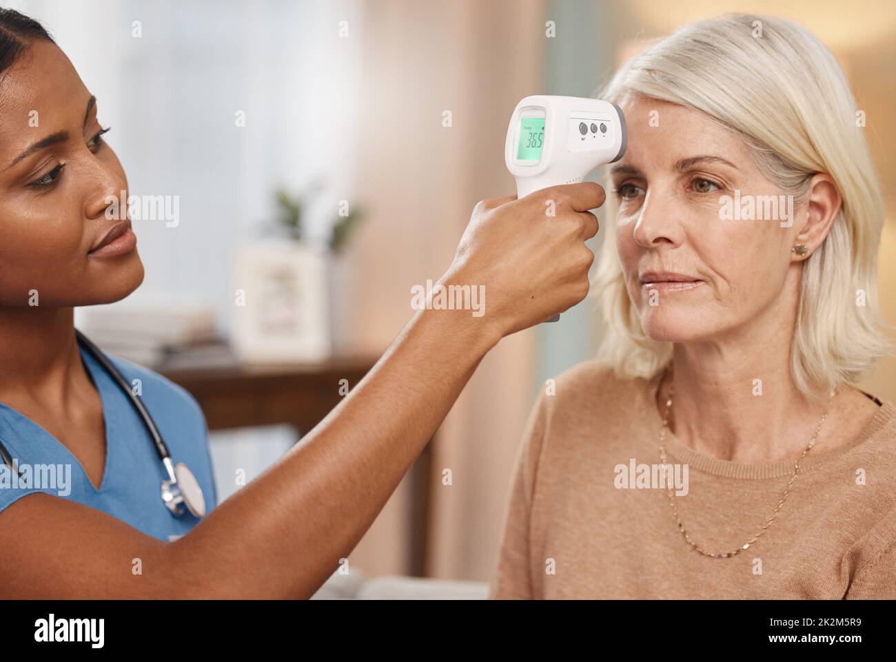 Lascia iniziare il vostro fisico ma prima un controllo di febbre. Shot di un medico che esamina una donna matura con un termometro a casa. Foto Stock