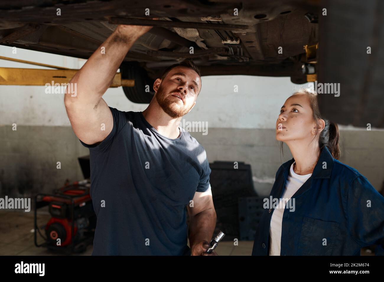 Il servizio di prima qualità è il nostro principale settore automobilistico. Colpo di due meccanici che lavorano insieme sotto una macchina sollevata. Foto Stock