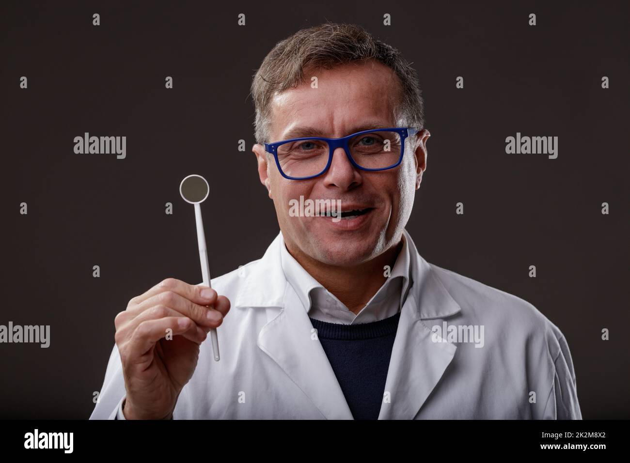 Dentista sicuro che mostra uno specchio dentale per il check-up regolare Foto Stock