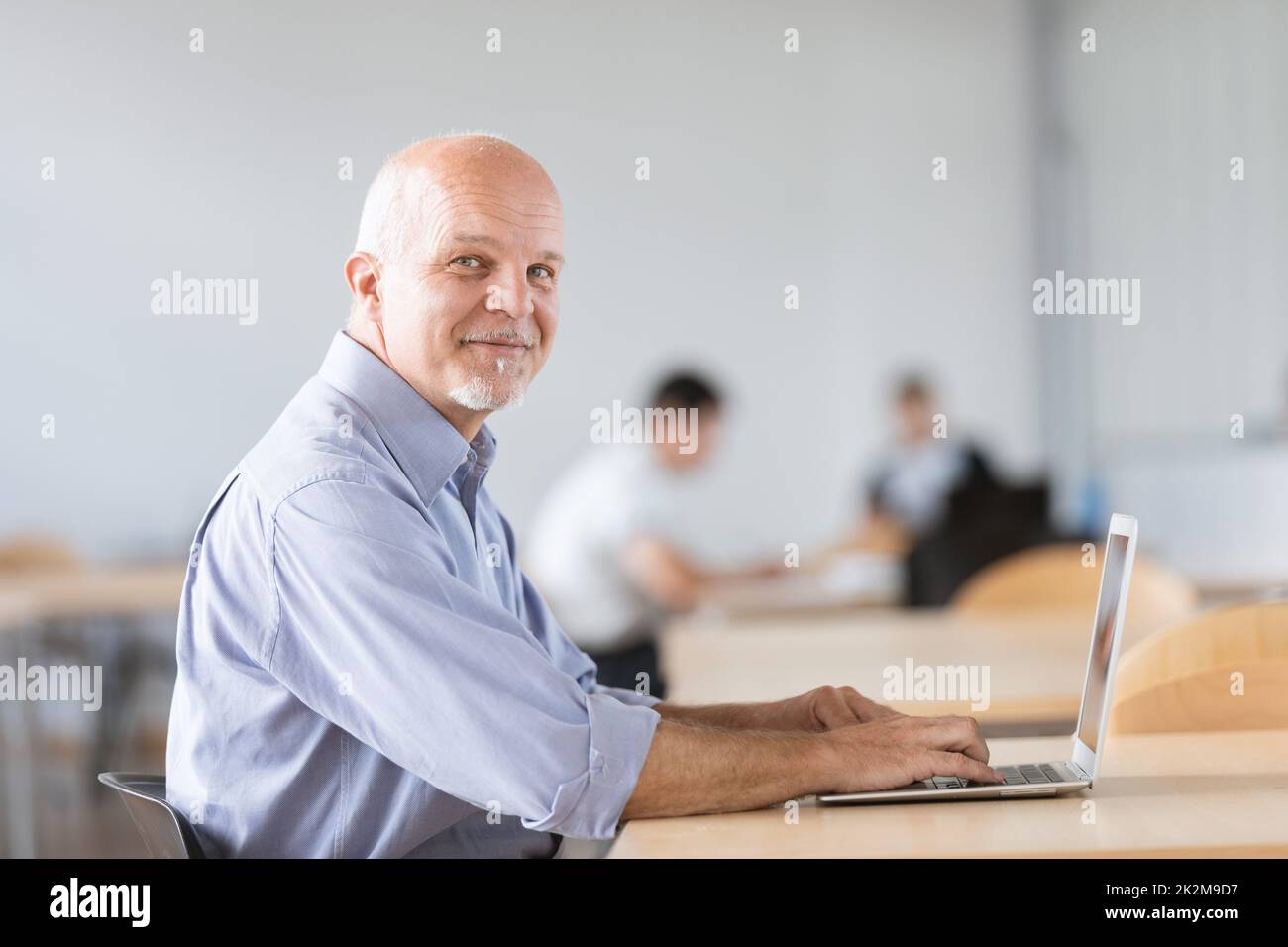 uomo maturo seduto e guardando la fotocamera mentre lavora sul notebook Foto Stock