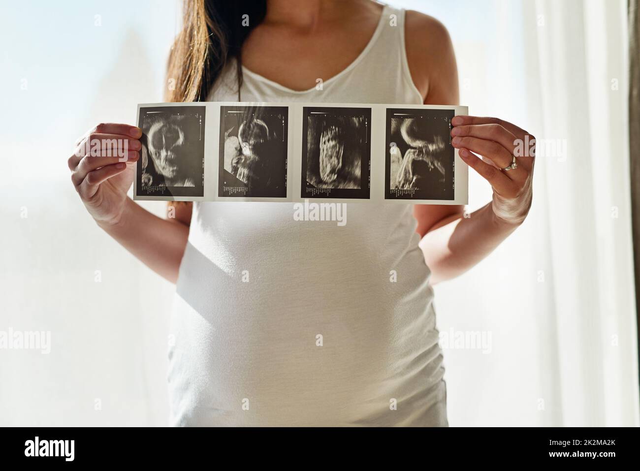 Primo ritratto di Babys. Scatto di una donna incinta non identificabile che tiene su una serie di immagini di ultrasuono davanti ad una finestra nel paese. Foto Stock