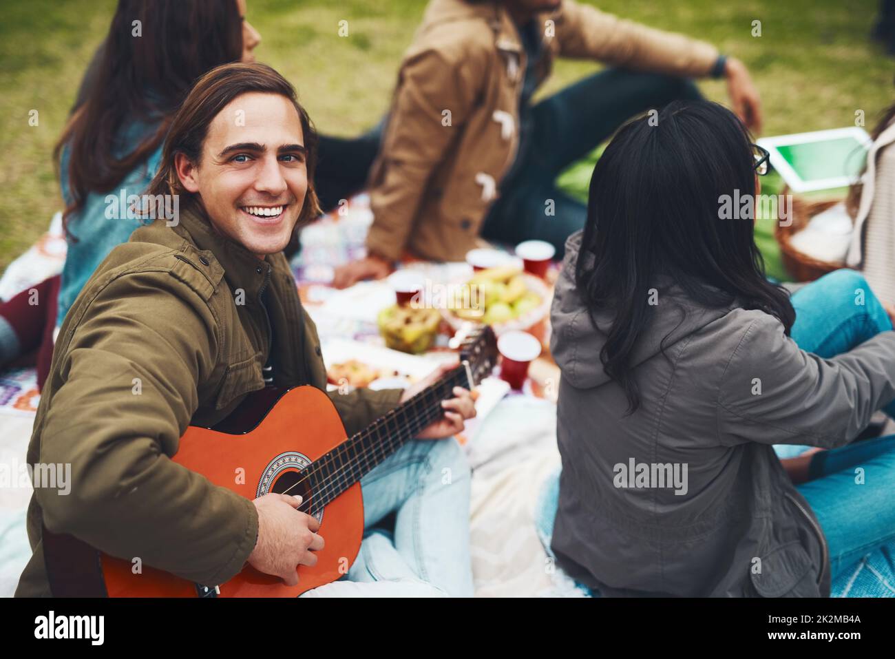 È il momento di riprodurre alcuni brani. Ritratto di un giovane allegro che sta per suonare la chitarra in un picnic con i suoi amici all'aperto durante il giorno. Foto Stock