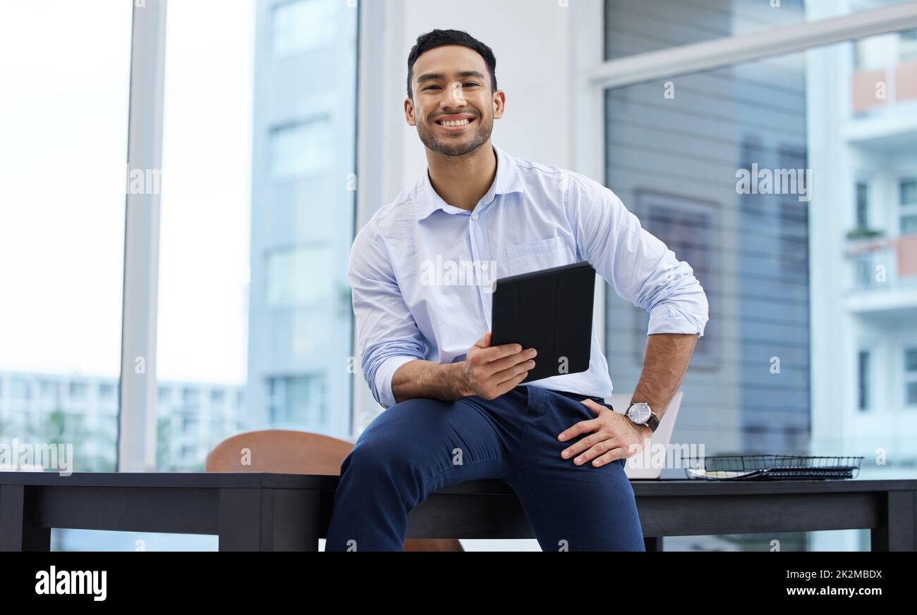 Il mio nome sarà parlato in camere in tutto il mondo. Scatto di un bel giovane uomo d'affari seduto da solo nel suo ufficio e in possesso di un tablet digitale. Foto Stock