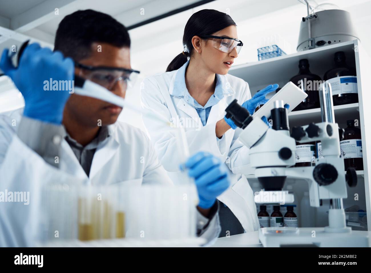 Duro al lavoro in nome della salute. Scatto di due giovani scienziati che utilizzano un tablet digitale mentre conducono la ricerca medica in un laboratorio. Foto Stock