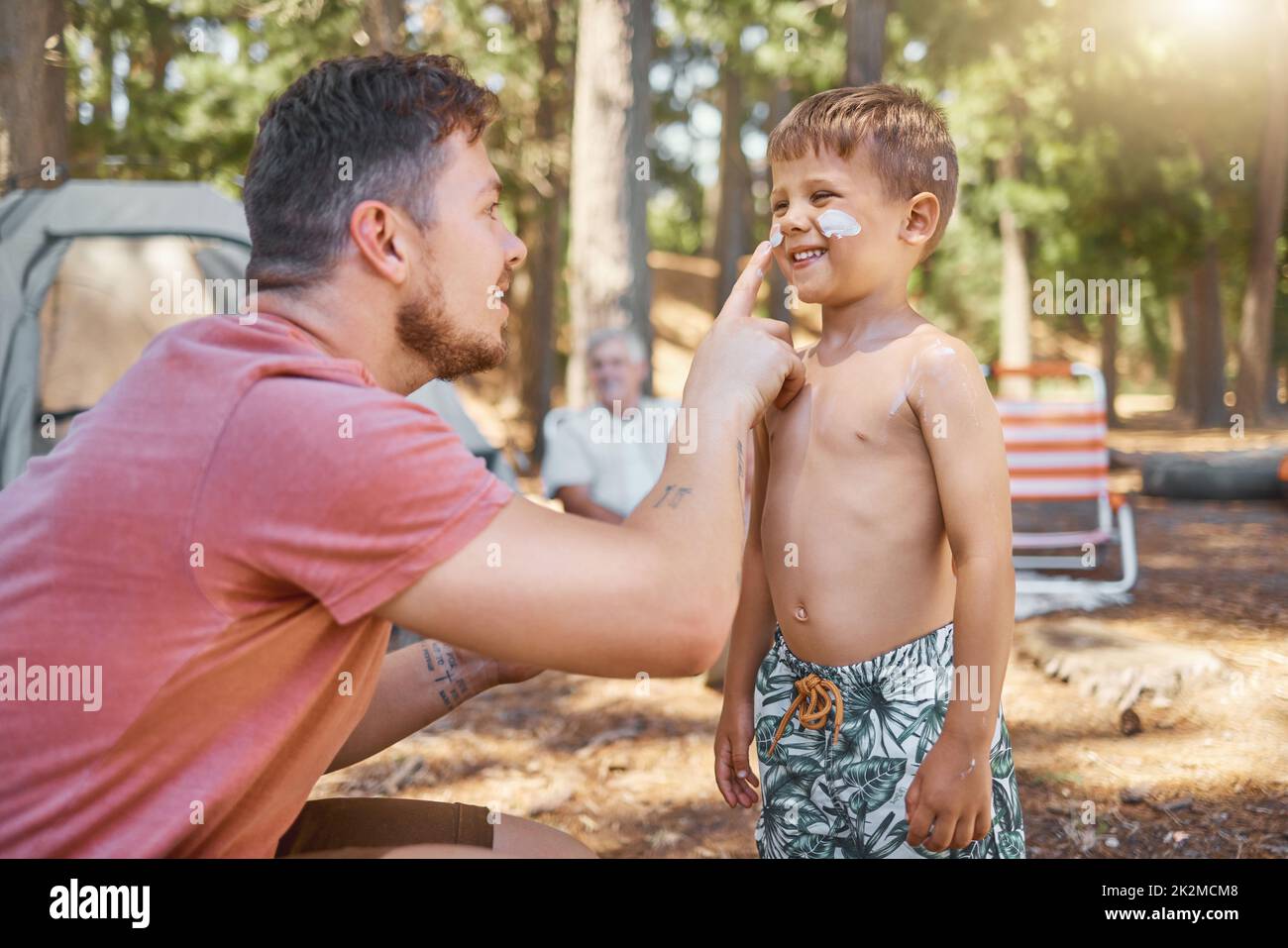 Non dimenticare la crema solare. Scatto corto di un bel giovane uomo che mette la crema solare sul suo adorabile figliolo mentre si accampano nei boschi. Foto Stock