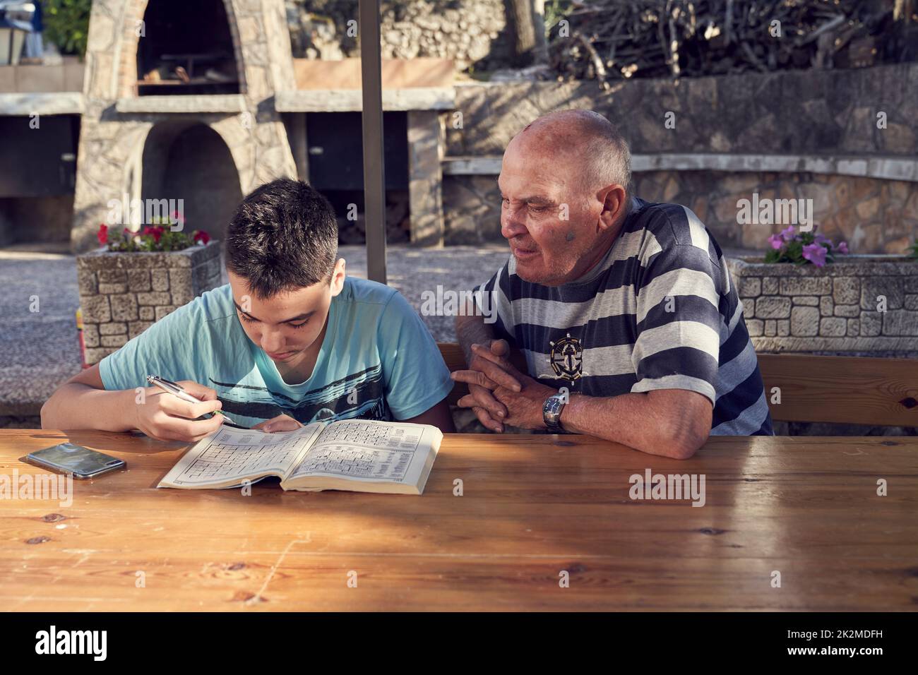 Un uomo anziano seduto a fare hobby a parole incrociate con suo nipote. Foto Stock