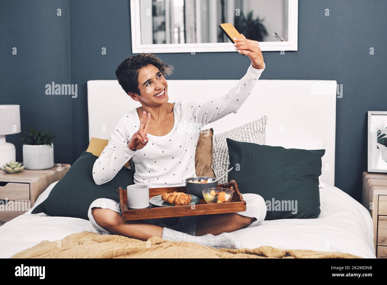 La vita di un blogger. Scatto a tutta lunghezza di una giovane donna attraente che prende un selfie mentre si posa con il suo vassoio per la colazione a letto. Foto Stock