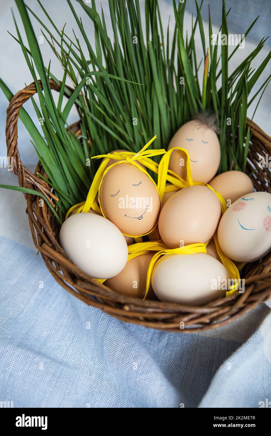 Belle uova di Pasqua dipinte con un viso carino, che giacciono in un cesto di legno insieme all'erba verde. Cartolina di Pasqua. Foto Stock