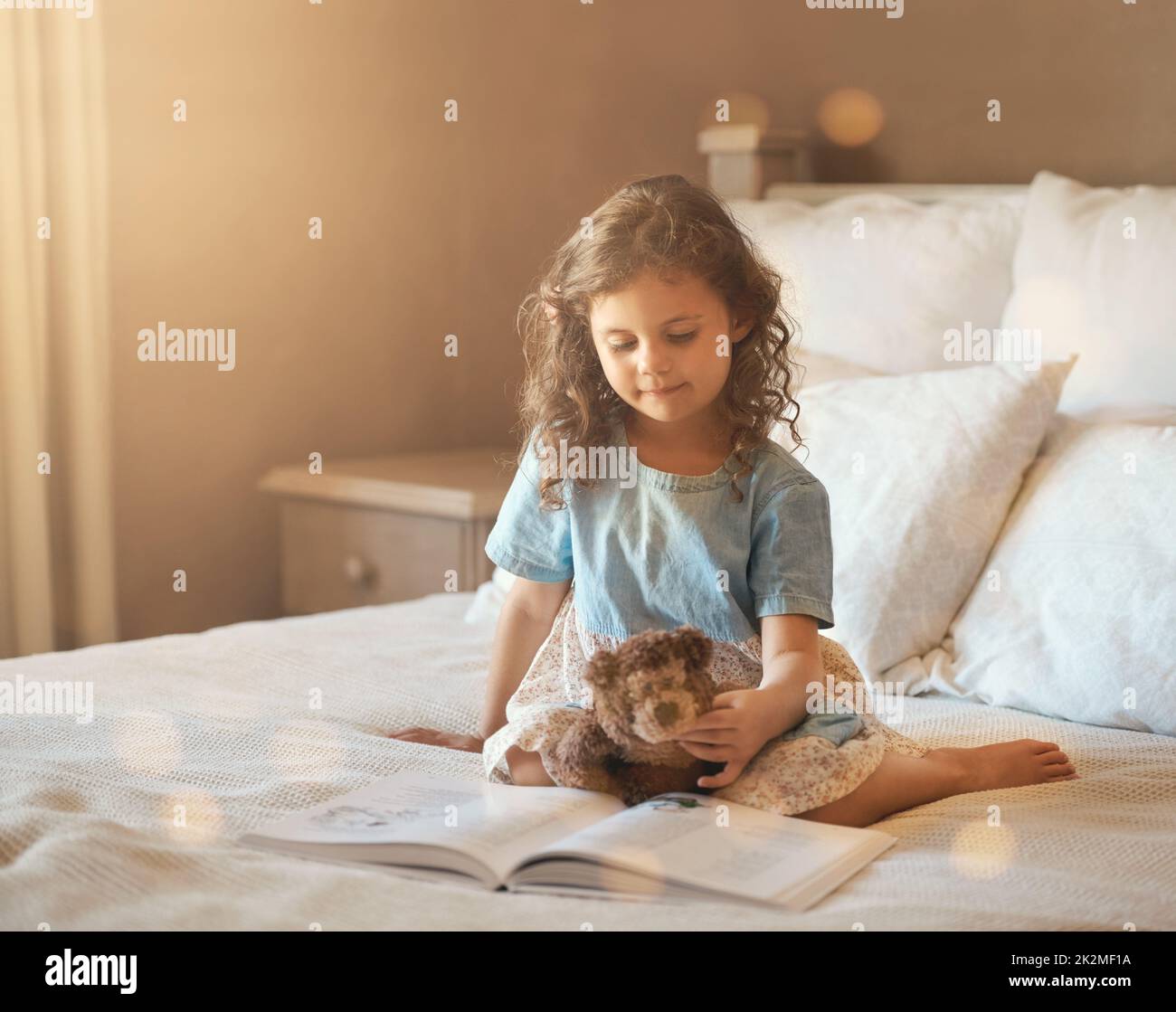 I libri sono importanti per i bambini. Scatto di una bambina adorabile a casa che legge un libro di storia sul suo letto con il suo orsacchiotto. Foto Stock