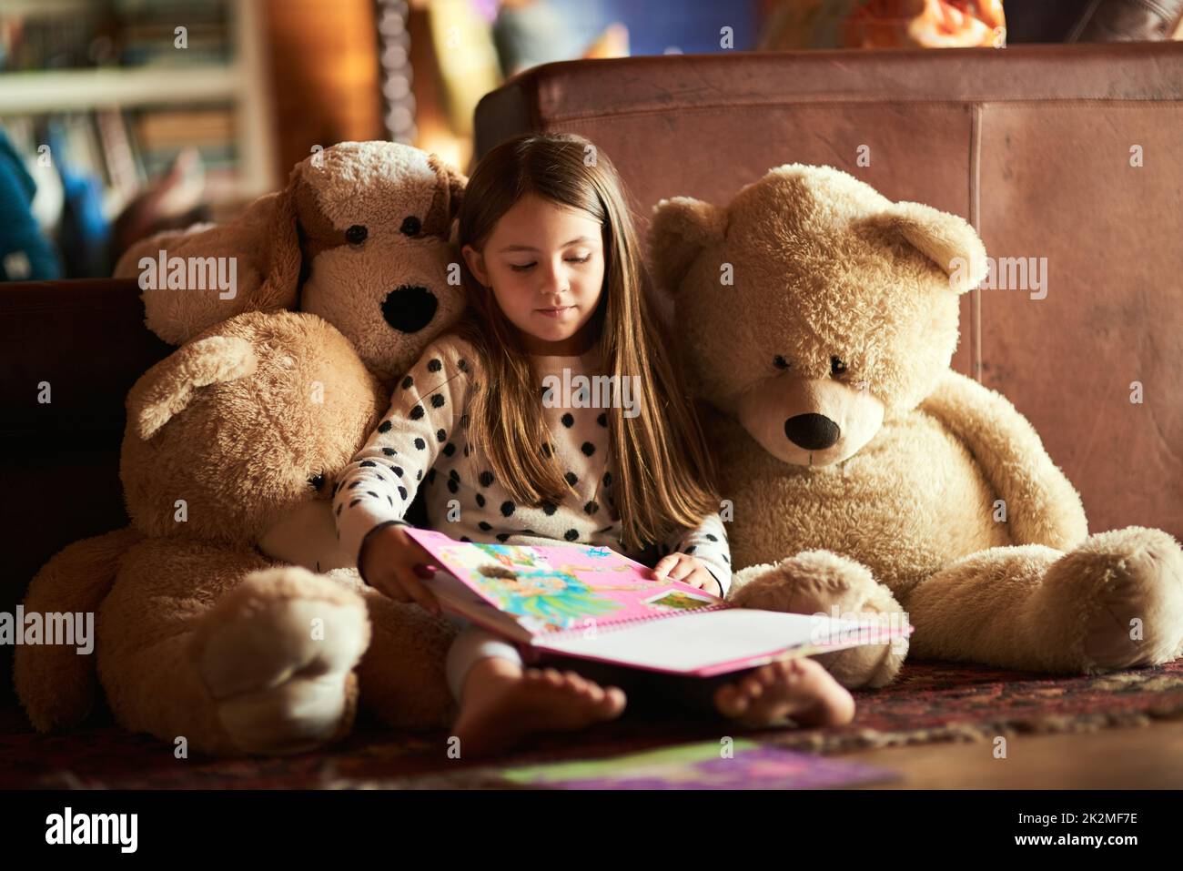 Leggere i suoi teddie una storia. Shot di una bambina che legge un libro con i suoi orsacchiotti intorno a lei. Foto Stock