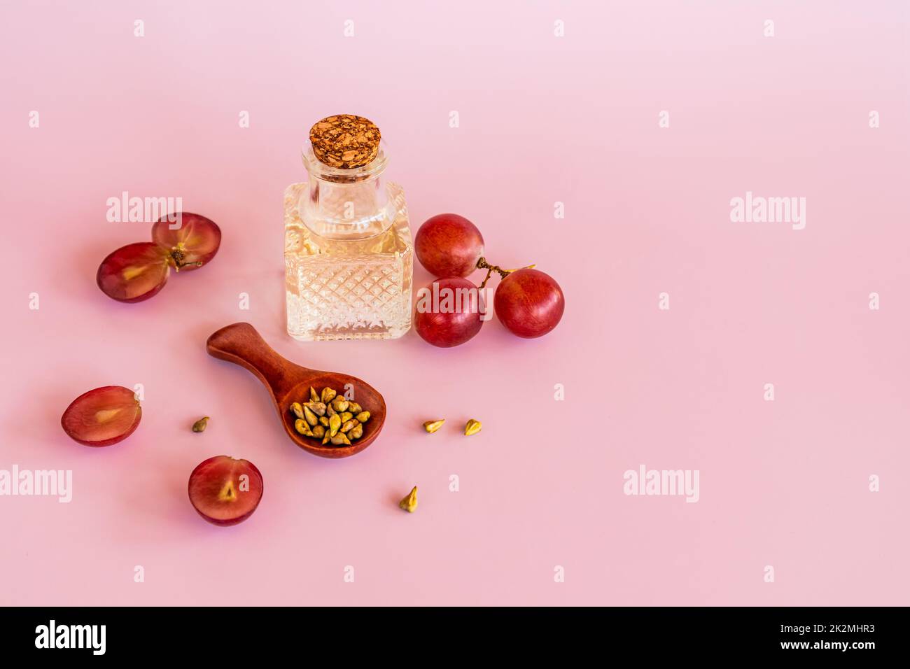 olio naturale di semi d'uva in una bella bottiglia con coperchio su fondo rosa tra bacche rosse e semi d'uva. cura biologica Foto Stock