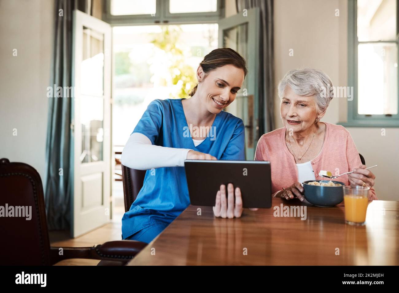 Scopri quanto è facile da usare. Scatto di una giovane infermiera e di una donna anziana utilizzando un tablet digitale all'ora di colazione in una casa di cura. Foto Stock