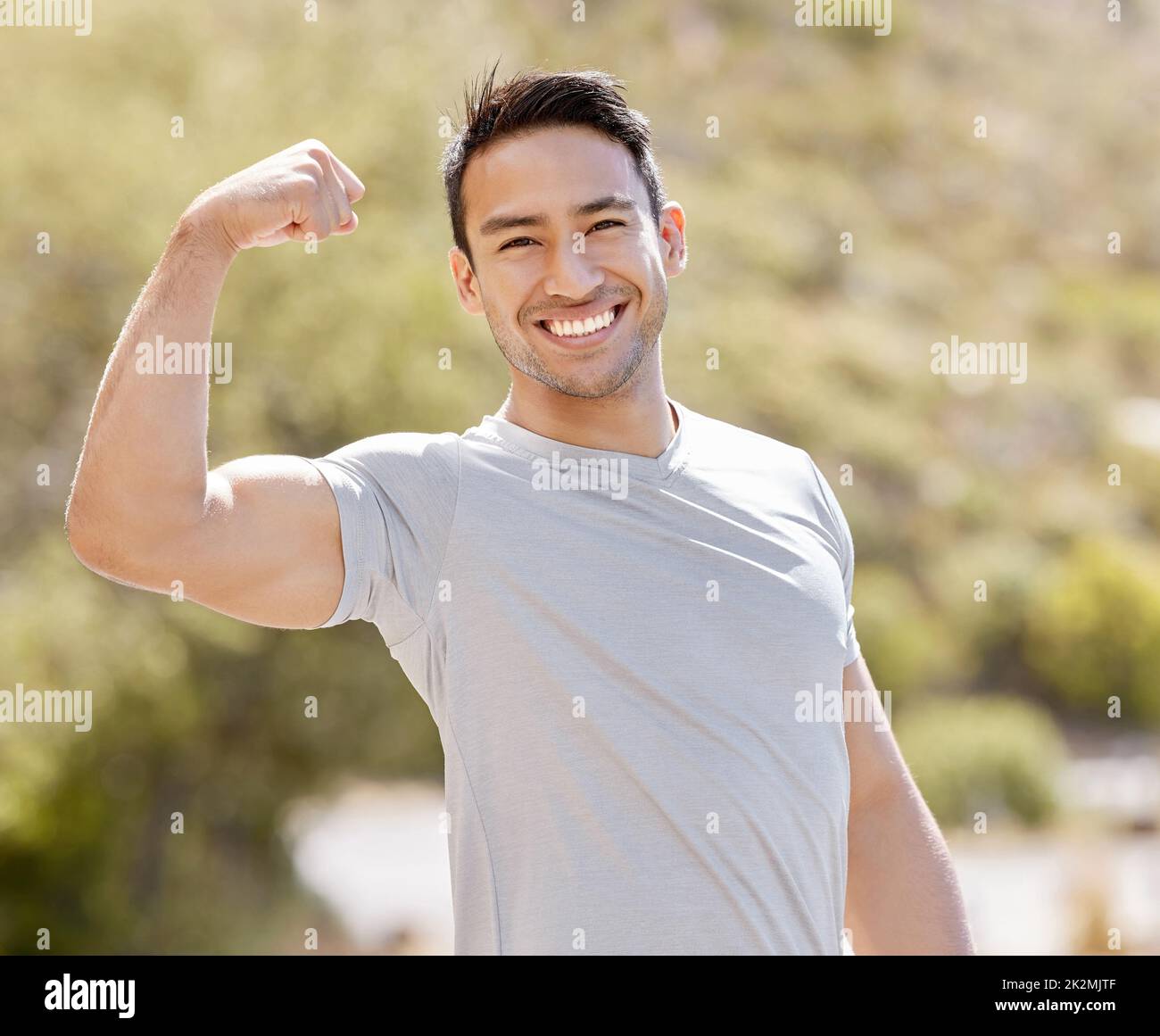 Fitness, natura e un uomo flexing bicipiti con un sorriso mentre si allenano nel parco all'aperto. Potenza, flessibilità e allungamento prima dell'allenamento o della corsa. Benessere, sport Foto Stock