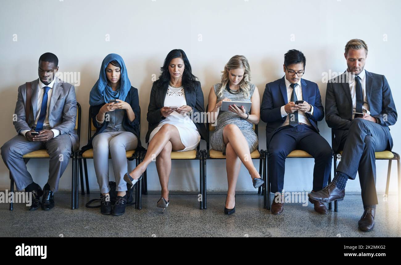 Rimanere connessi mentre aspettano. Girato di un gruppo di uomini d'affari ben vestiti utilizzando i loro smartphone, in attesa di essere intervistati. Foto Stock
