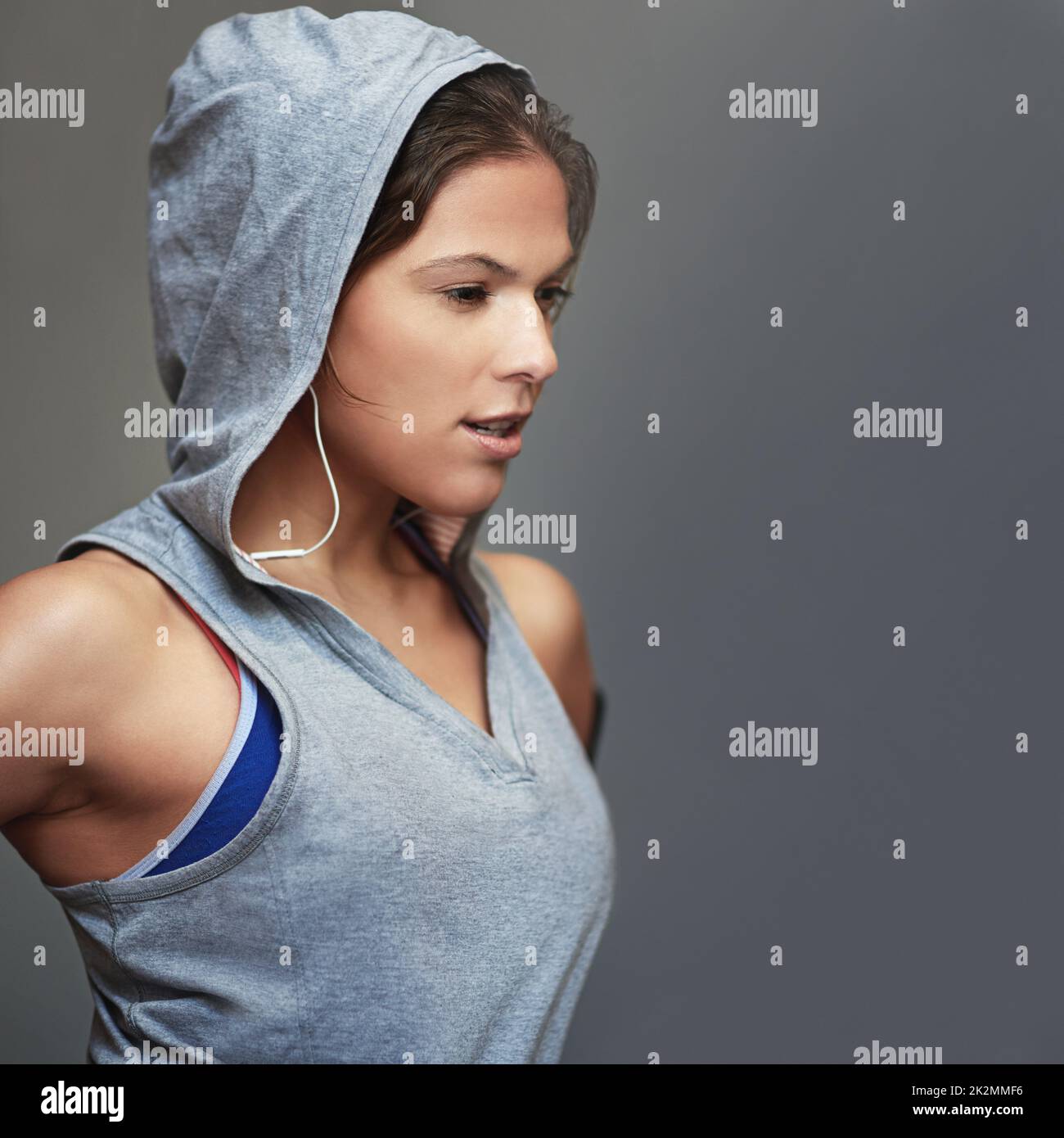 Si impegna per il fitness. Scatto di una giovane donna sportiva che indossa una felpa con cappuccio in posa su sfondo grigio. Foto Stock