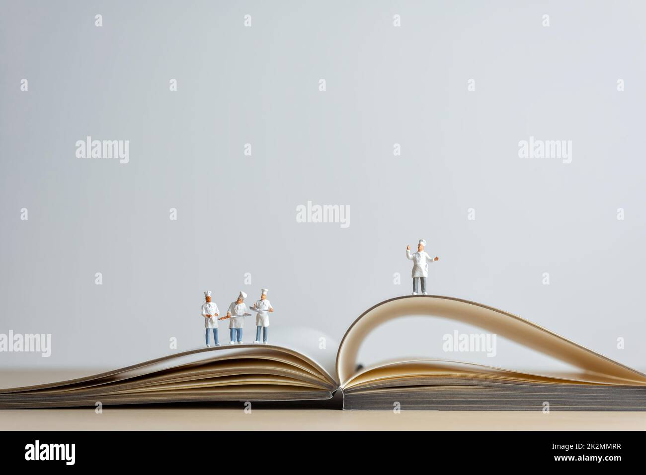 Chef in miniatura in piedi sulla parte superiore aperta del libro di ricette. Concetto di cucina a vista Foto Stock