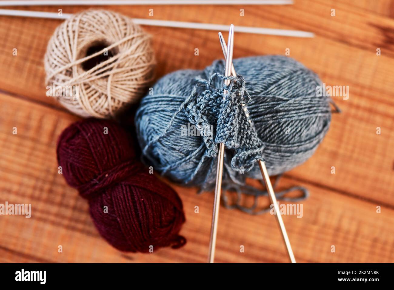 Tutti vogliono un maglione di Natale quest'anno. Foto vita di polpette di lana multicolore e penne per maglieria su un tavolo di legno. Foto Stock