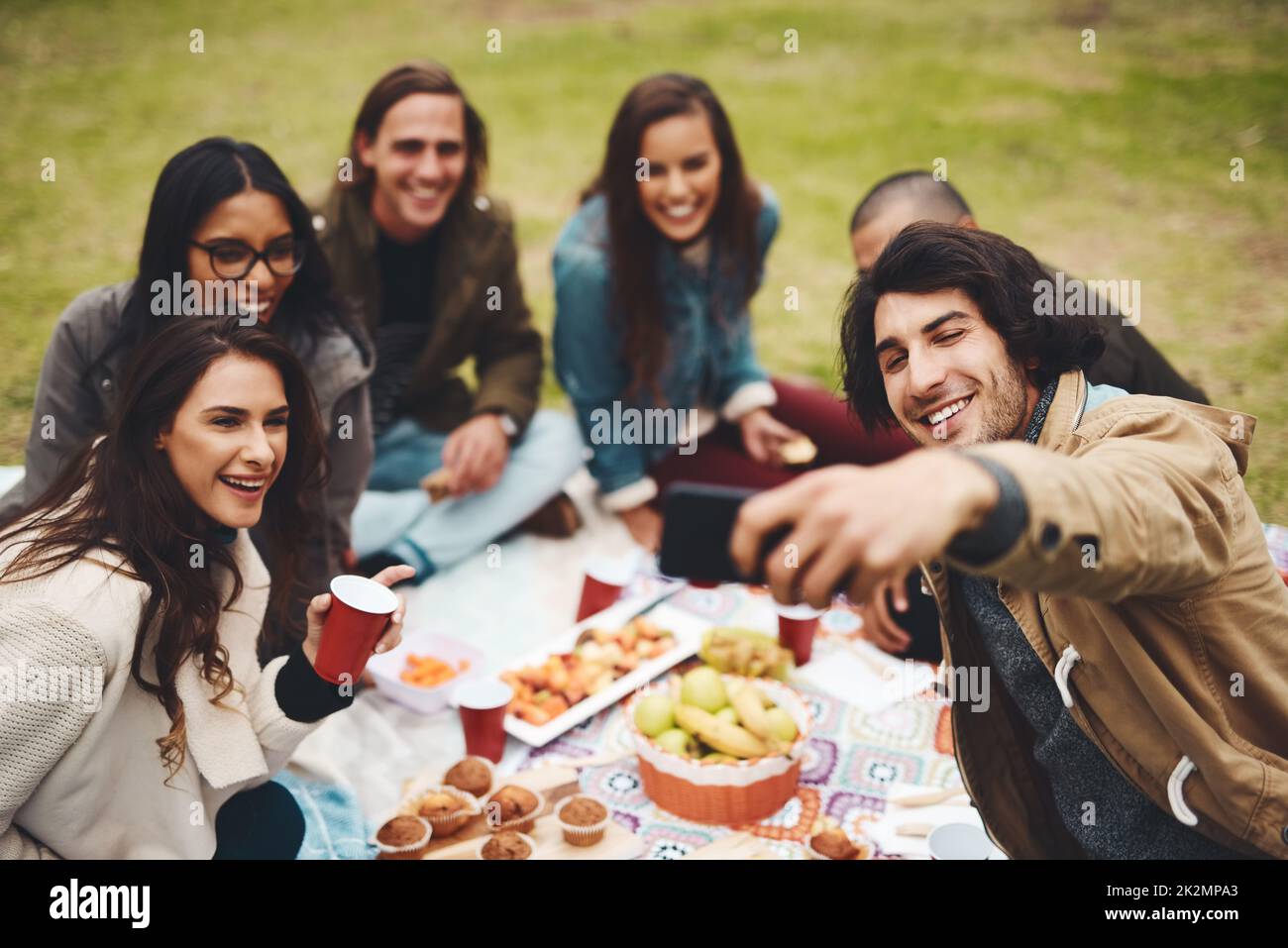Tutti si fanno per la foto. Foto di un gruppo di giovani amici che prendono un autoritratto insieme mentre si tiene un picnic all'aperto durante il giorno. Foto Stock