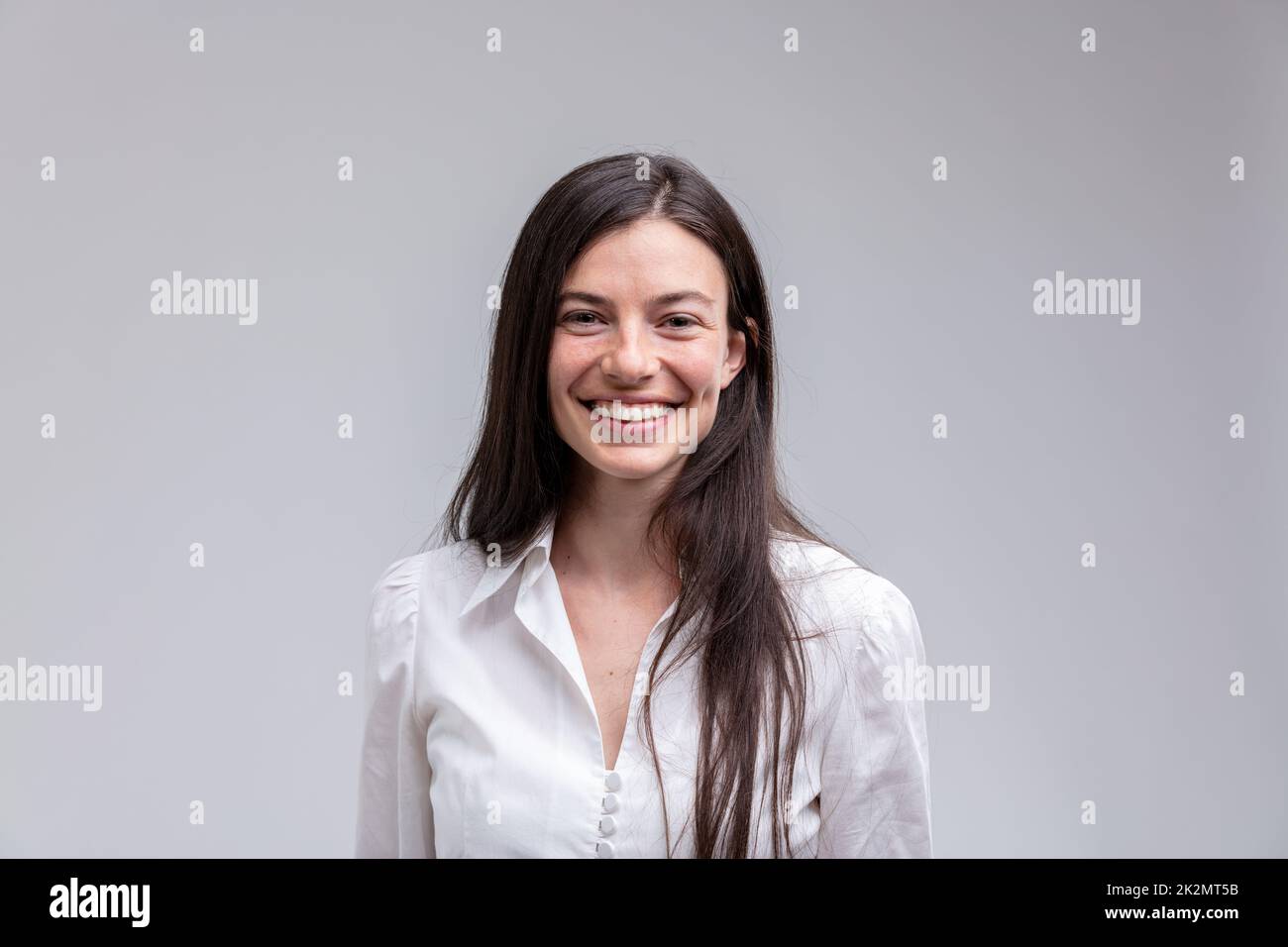 Giovane donna sorridente dai capelli lunghi in camicia bianca Foto Stock