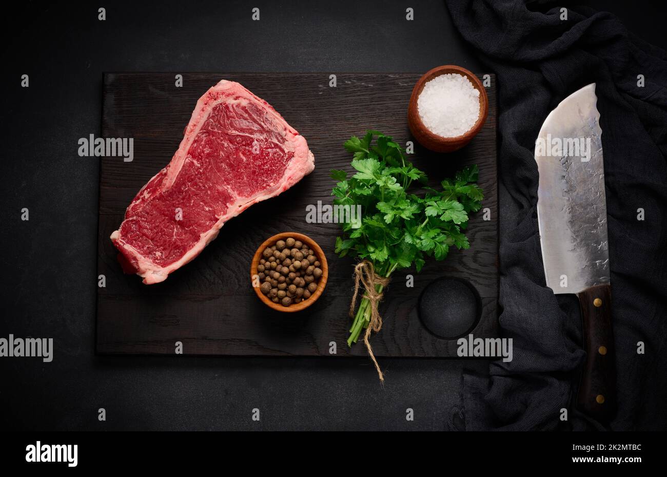 Pezzo fresco di carne di manzo crudo, bistecca striploin su sfondo nero, vista dall'alto. Pezzo marmorizzato di carne New York Foto Stock