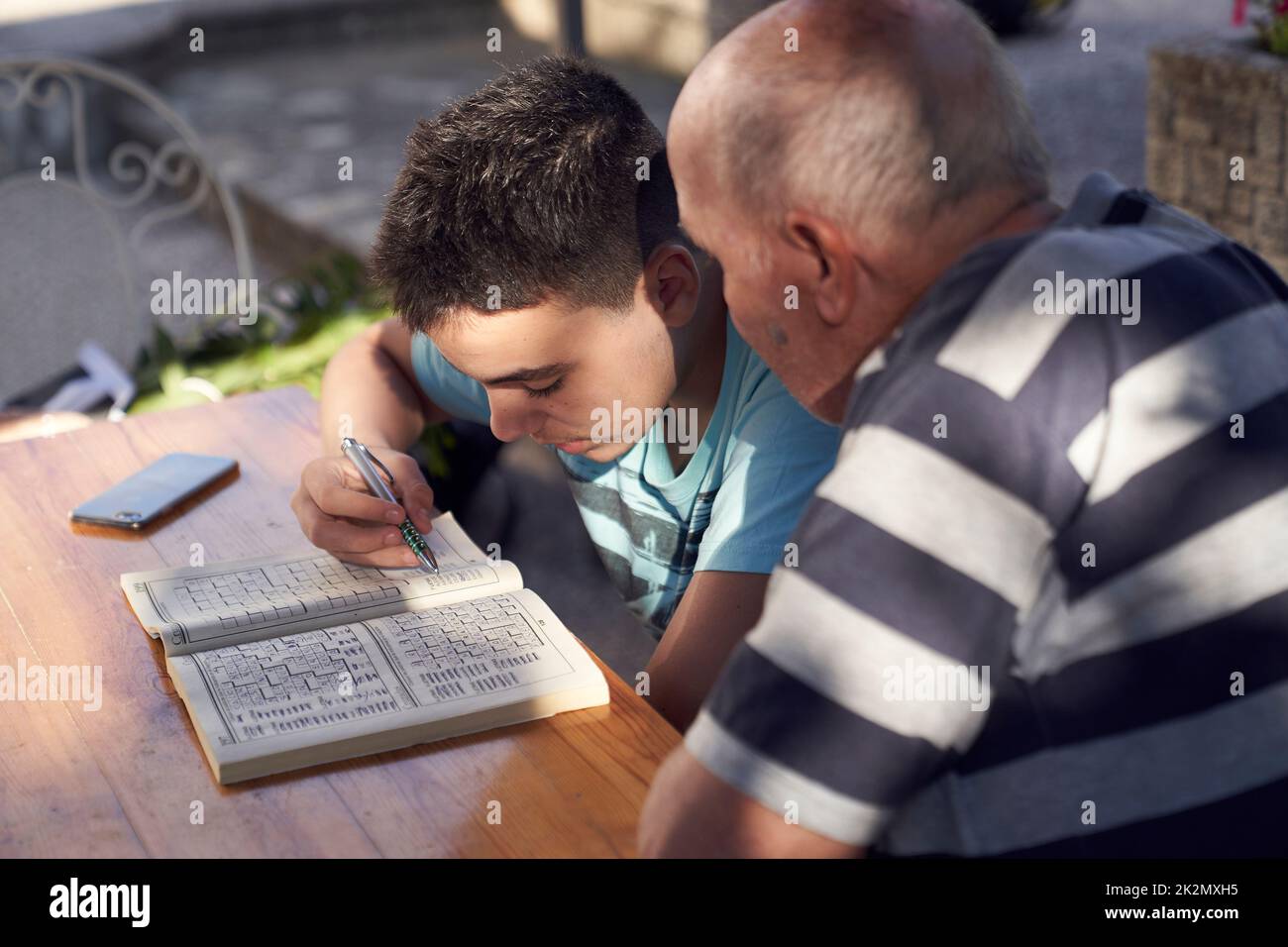 Un uomo anziano seduto a fare hobby a parole incrociate con suo nipote. Foto Stock
