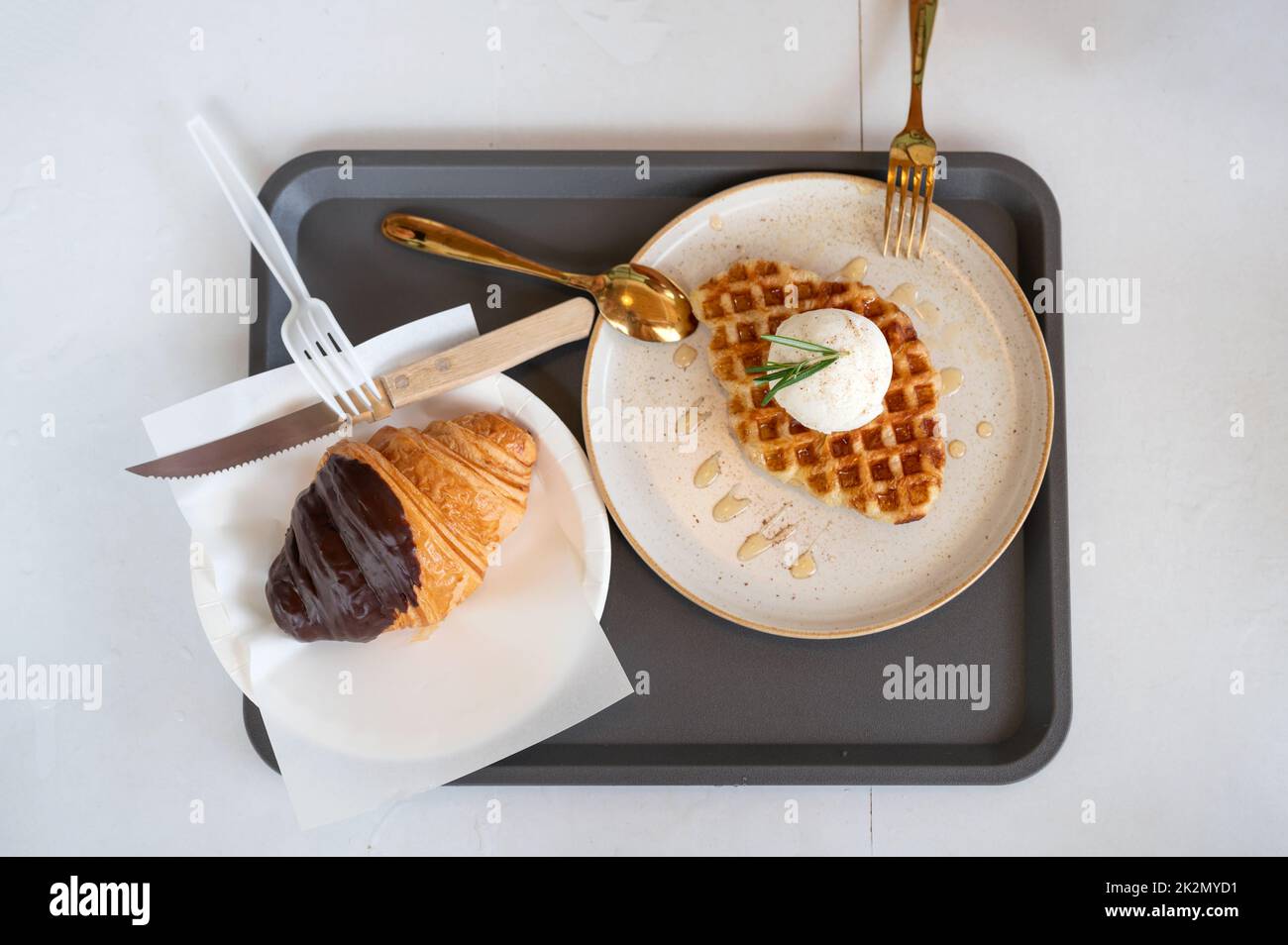 Vista dall'alto del gelato alla vaniglia con cialde e croissant al cioccolato e cucchiaio di ottone su piatto bianco Foto Stock