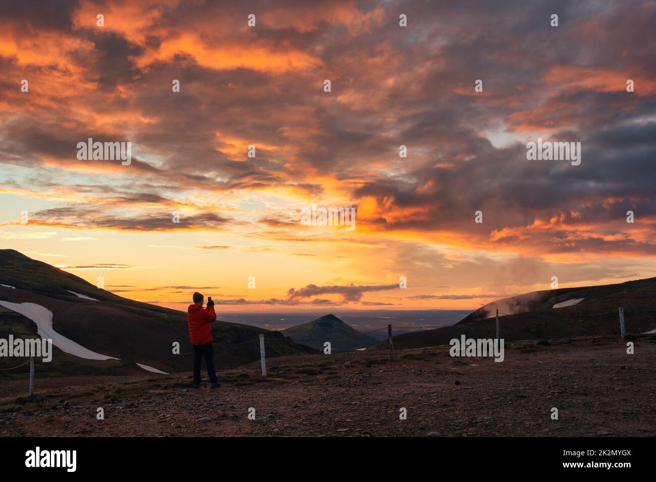 L'uomo del turismo che si gode e scatta foto con lo smartphone con il cielo colorato sopra la montagna vulcanica nelle alture islandesi in estate in Islanda Foto Stock