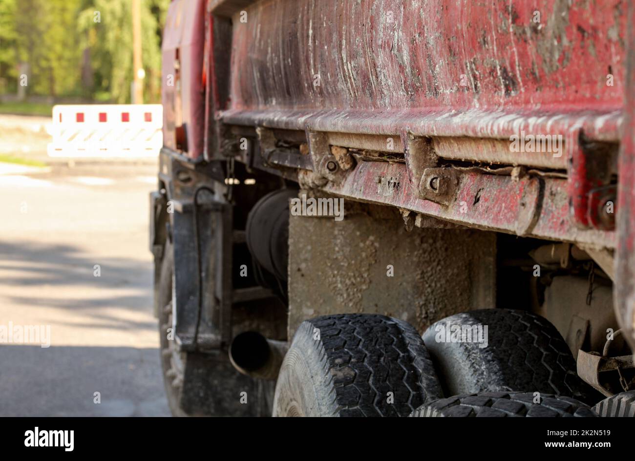 Primo piano del vecchio lato del camion arrugginito e sporco, sverniciatura sulla parete del vano di carico, pneumatici grandi visibili, distanza del segnale di identificazione del blocco stradale sfocata. Illustrazione dei lavori su strada. Foto Stock